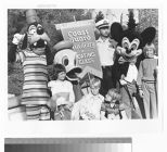 Disney mascots Mickey Mouse, Donald Duck, and Goofy standing with four children and a U.S. Coast Guard Auxiliary member